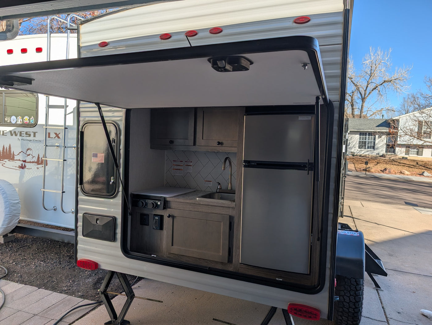 Rear view of an RV rental travel trailer with its outdoor kitchen hatch open, revealing a built-in sink, stove, and refrigerator. — photo 20