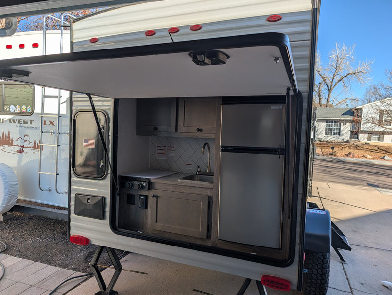 Rear view of an RV rental travel trailer with its outdoor kitchen hatch open, revealing a built-in sink, stove, and refrigerator. — photo 20