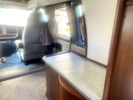 Bright rv rental interior, featuring a tan front seat, side window with curtains, and a speckled countertop.