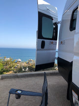 Winnebago Solis rv rental with open doors, offering a serene ocean view from a scenic campsite.