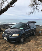 Dark blue Dodge Caravan minivan parked on a rocky Hawaiian coast with open hatch, great for an RV rental trip.