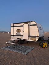 Experience beach camping with this Coleman rv rental. Setup includes a generator, picnic table, and rug on sandy ground under a clear sky.