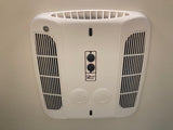 This white, ceiling-mounted Coleman Mach AC unit, common in RV rentals, offers climate control via its knobs and adjustable vents.