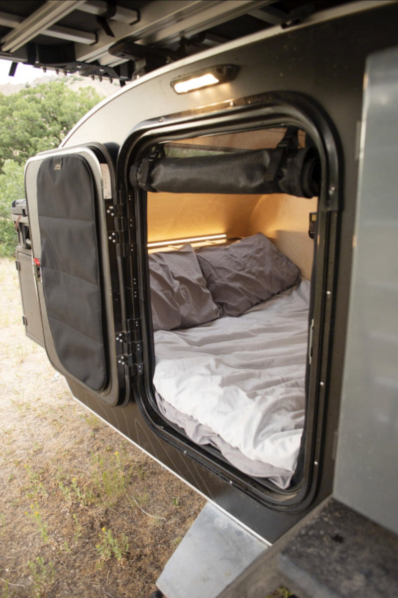 Inside this RV rental, a compact sleeping area features a bed with cozy bedding & warm lighting. — photo 12