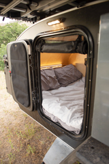 Inside this RV rental, a compact sleeping area features a bed with cozy bedding & warm lighting.