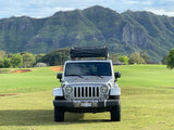 Parked on Kauai, a silver Jeep with a rooftop tent faces lush mountains. Perfect for your outdoor RV rental experience.