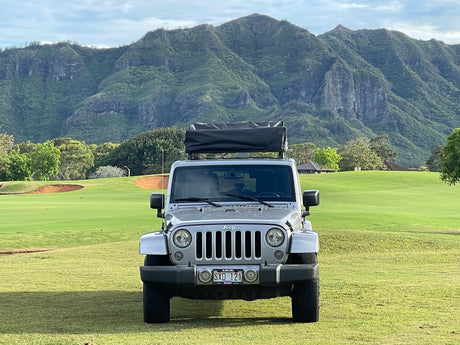 Parked on Kauai, a silver Jeep with a rooftop tent faces lush mountains. Perfect for your outdoor RV rental experience.