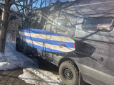 This grey RV rental camper van, equipped with a blue/white surfboard on its side, is parked in snow, ready for winter adventures.