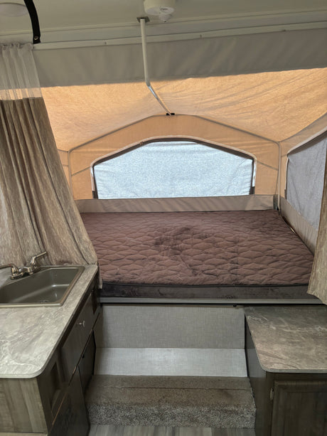 Interior of an rv rental pop-up camper with a large quilted bed, counter with sink, and fabric tenting for a cozy camping experience.
