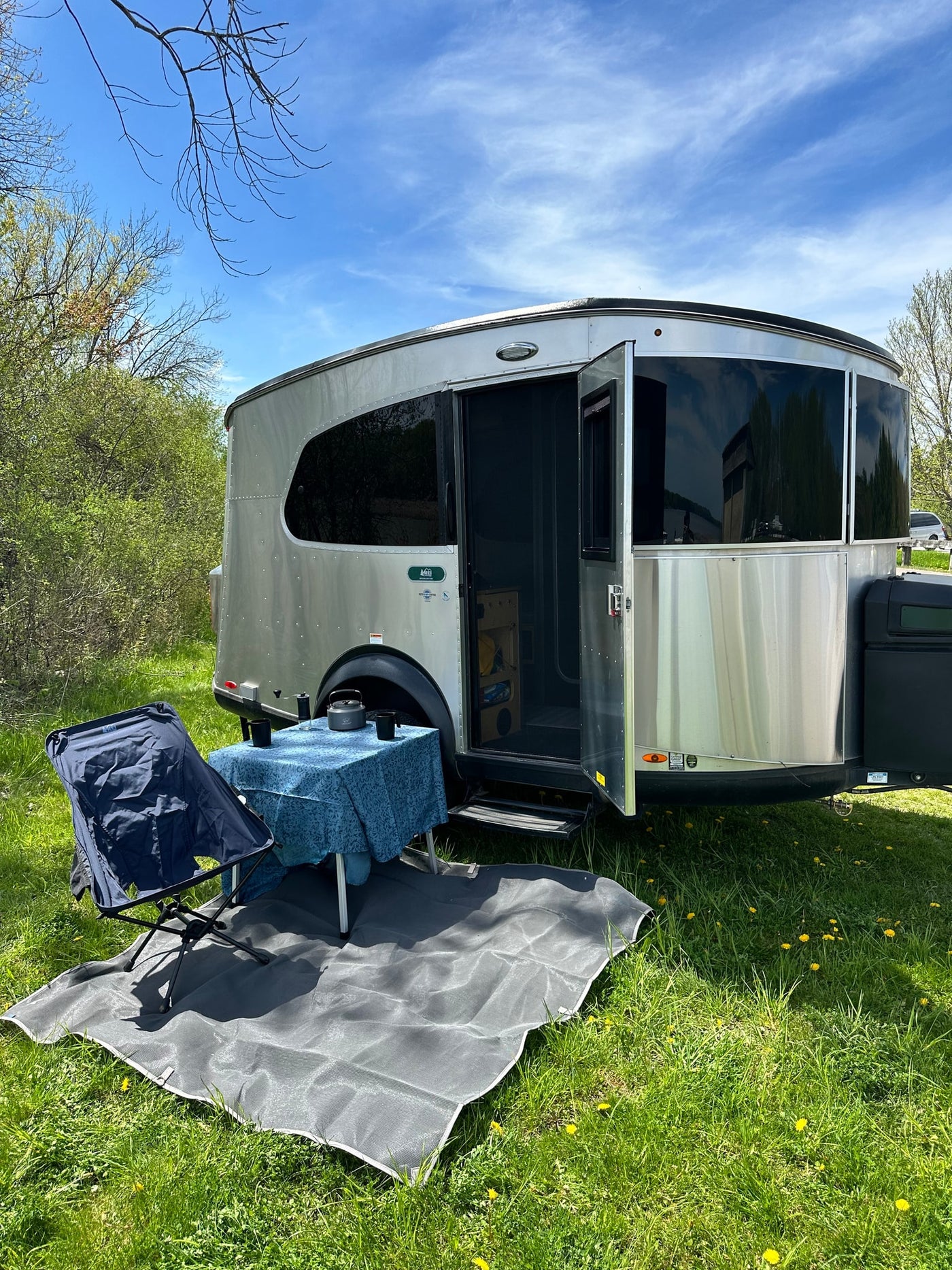 Experience nature in an rv rental: silver travel trailer with an open door, outdoor dining setup on green grass, under a blue sky.