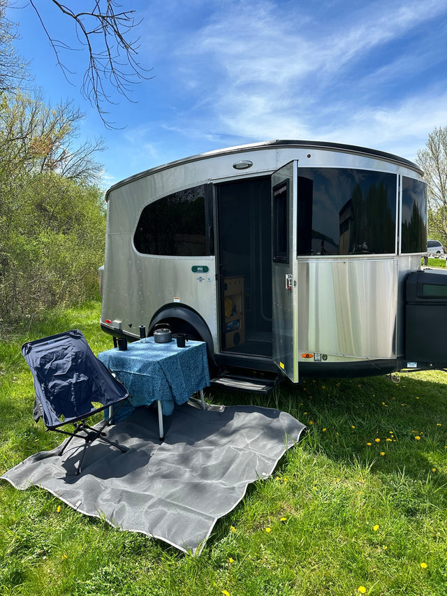 Experience nature in an rv rental: silver travel trailer with an open door, outdoor dining setup on green grass, under a blue sky.