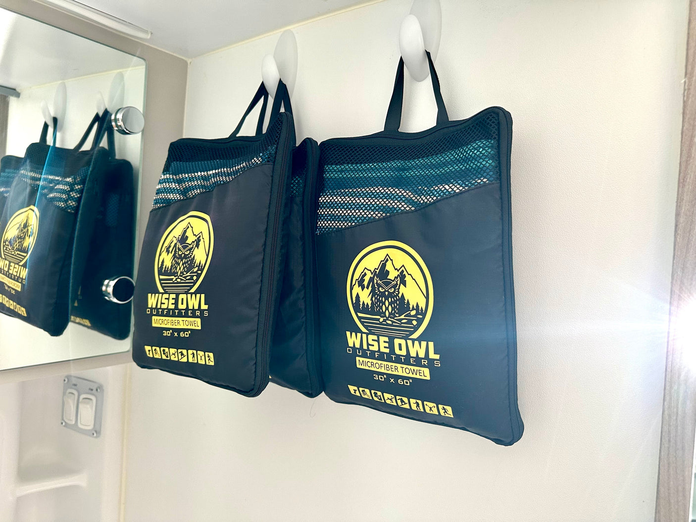 Two Wise Owl Outfitters microfiber towel bags hang on hooks inside an RV rental, ready for travel.