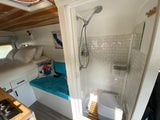 Modern RV rental interior featuring a cozy bed, compact kitchen, and a well-appointed shower and Dometic toilet.