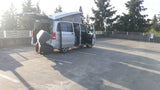Silver RV rental camper van with pop-top, open doors & rear cargo, parked in a sunny lot.