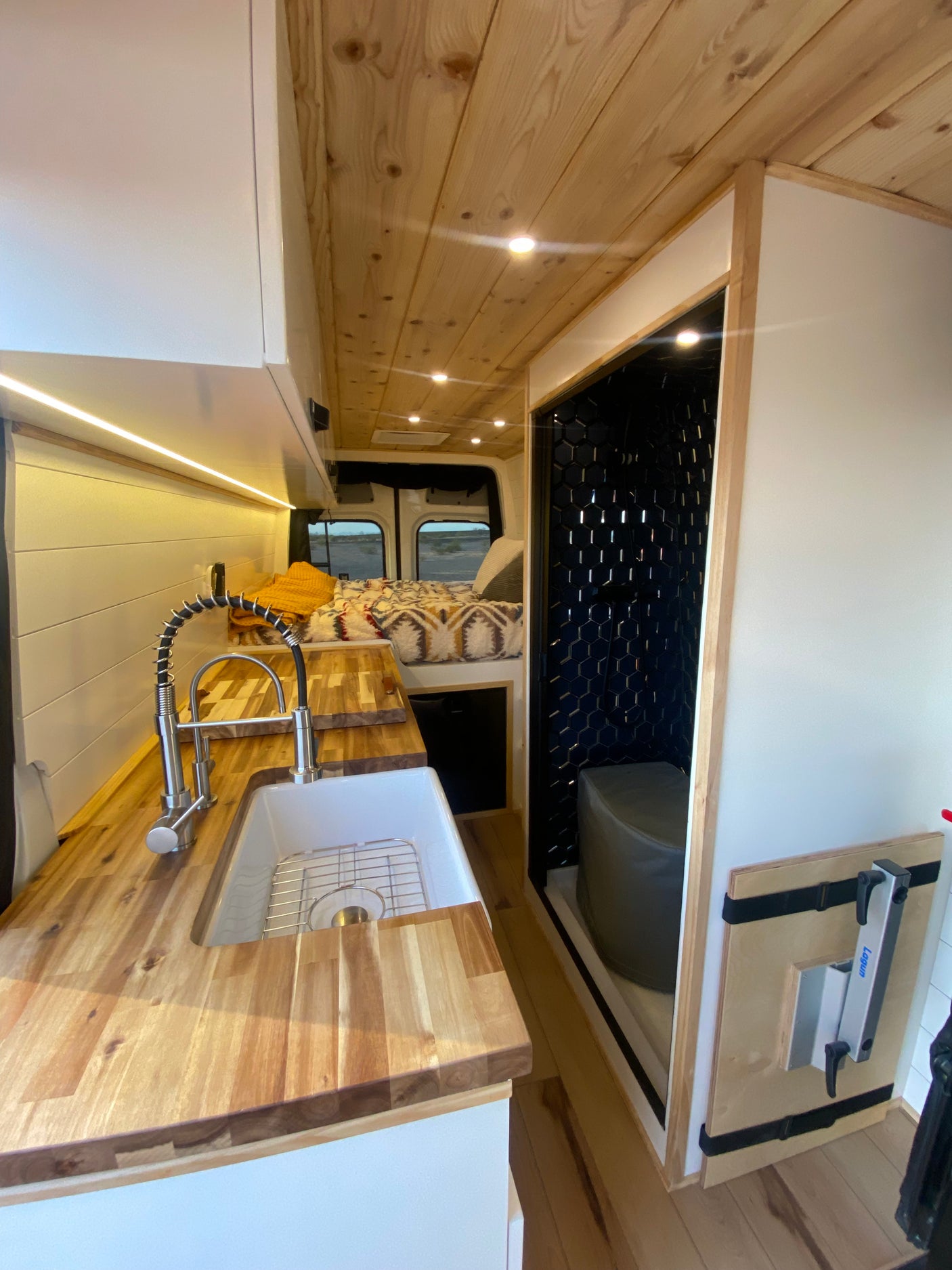 Explore this stylish rv rental camper van's interior: a wooden kitchen, cozy bed, and compact tiled bathroom.