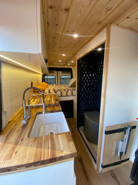 Explore this stylish rv rental camper van's interior: a wooden kitchen, cozy bed, and compact tiled bathroom.