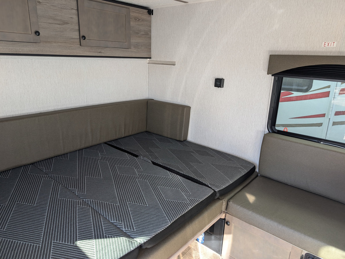 RV rental interior: Convertible dinette bed with modern patterned cushions, overhead storage, and window. Ideal for compact camper living. — photo 9
