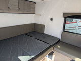 RV rental interior: Convertible dinette bed with modern patterned cushions, overhead storage, and window. Ideal for compact camper living.