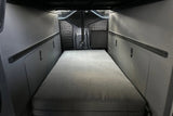 RV rental interior: A camper van's functional sleeping area with a grey mattress, flanked by modular wall panels and storage compartments.