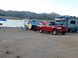 RV rental vehicles: Red pickup towing a Grand Ascape camper, and a Tiffin motorhome, parked by a lake and mountains.
