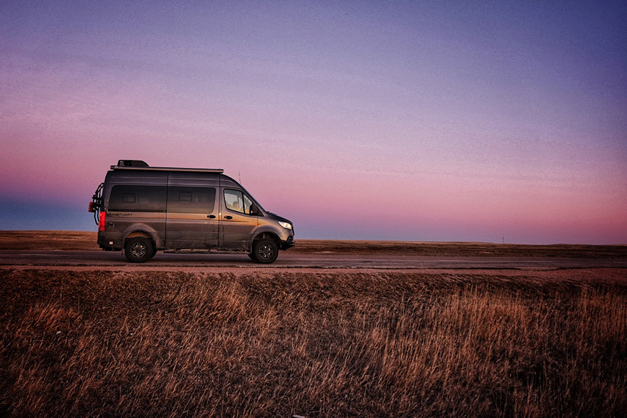 Grey camper van parked on a roadside under a vibrant sunset sky. Ideal for your next RV rental road trip!