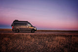 Grey camper van parked on a roadside under a vibrant sunset sky. Ideal for your next RV rental road trip!