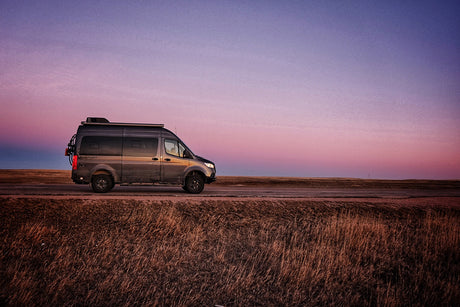 Grey camper van parked on a roadside under a vibrant sunset sky. Ideal for your next RV rental road trip!