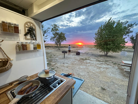 RV rental sunset cooking: sausages sizzle while watching vibrant outdoor views from the camper kitchen.