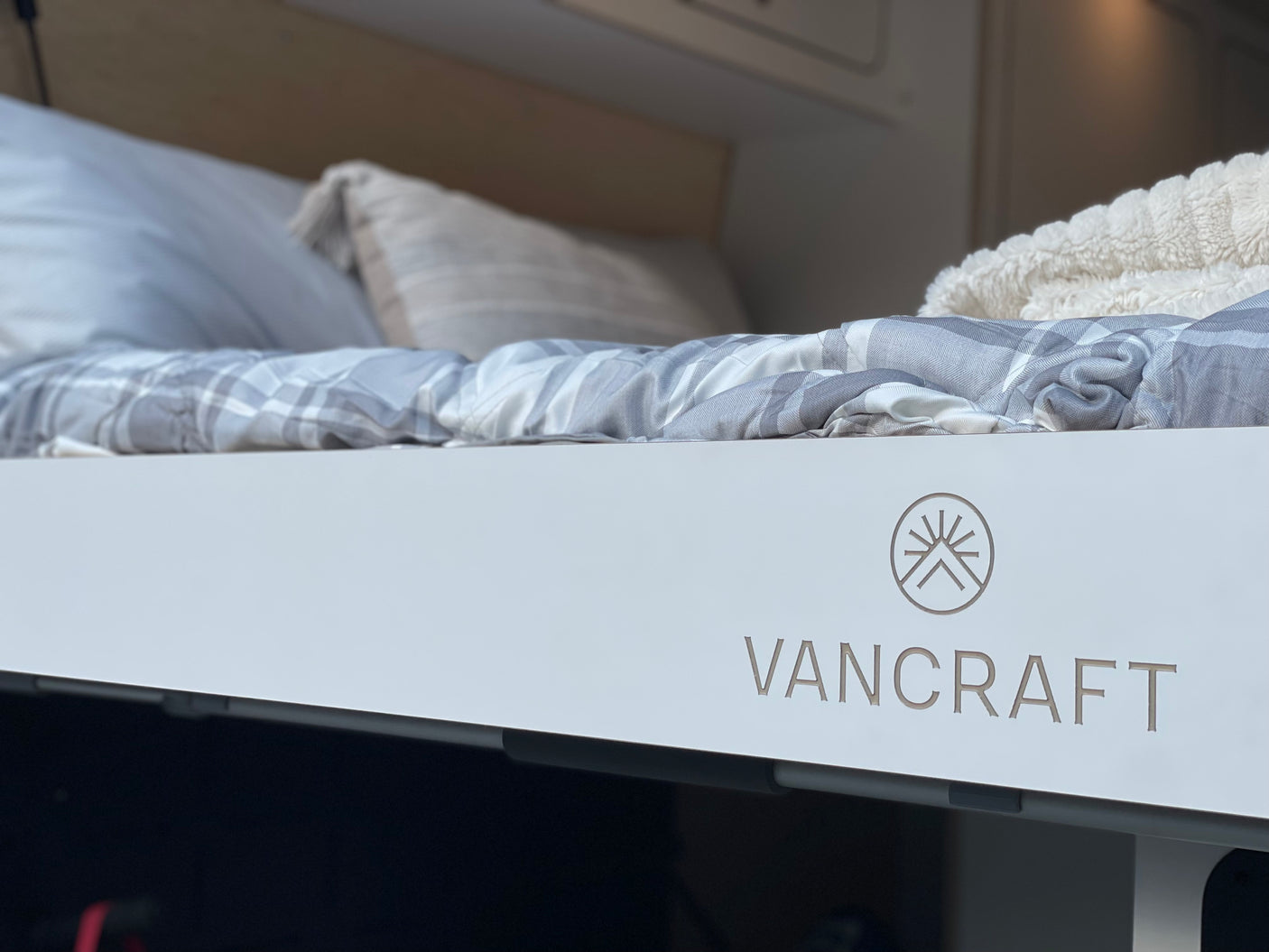 A neatly made bed with grey plaid bedding inside a VANCRAFT RV rental, ideal for comfortable travel.