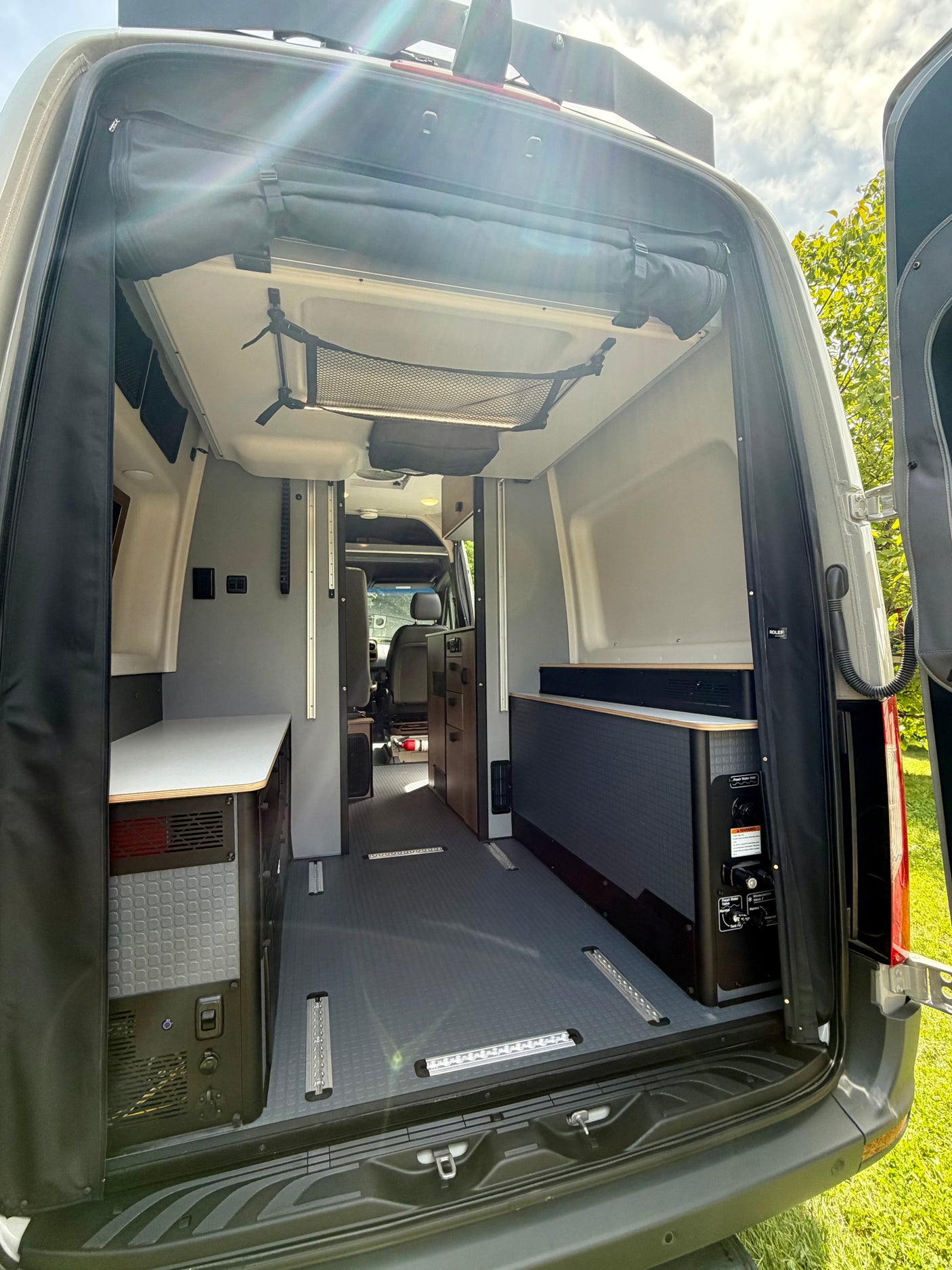 Rear view of an RV rental camper van interior: compact kitchen, utility panel, flexible floor tracks, and overhead storage.