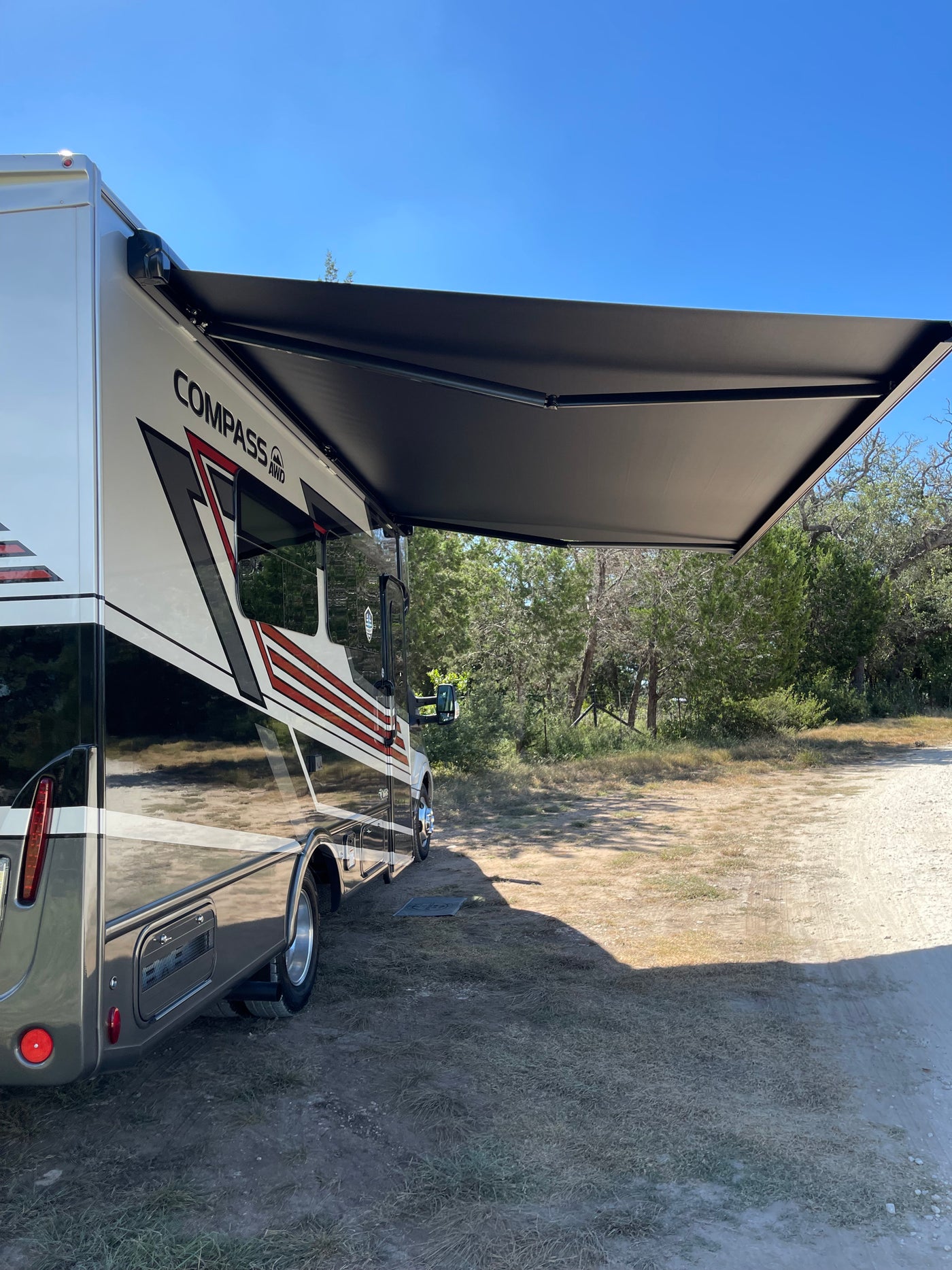 Compass AWD RV rental with extended black awning, parked on a sunny dirt campsite. — photo 10