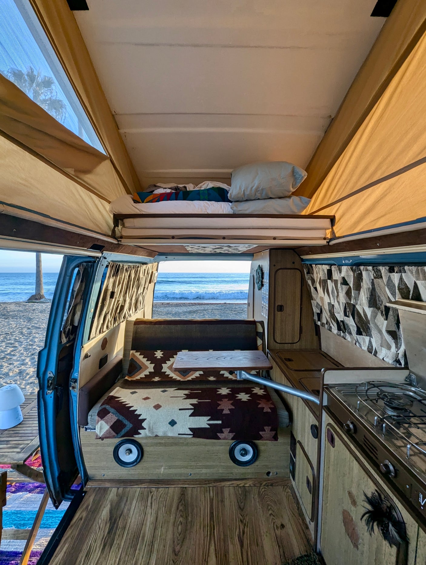 Cozy camper van interior, featuring a pop-top bed, kitchen, and ocean views from the doorway. Ideal for an rv rental.