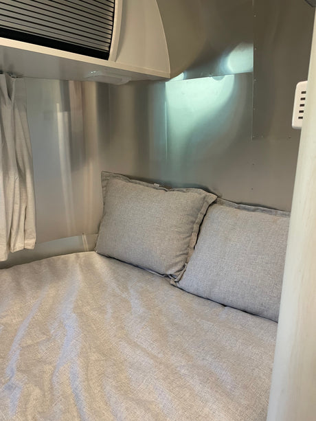 Cozy RV rental bed with light gray linen bedding and pillows, set within a sleek metallic travel trailer interior.