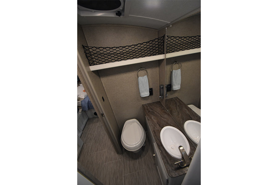 This RV rental features a compact bathroom with a toilet, sink, mirror, and convenient mesh overhead storage. — photo 17