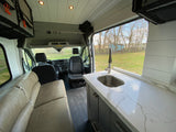 Spacious RV rental interior featuring a modern kitchenette with sink, comfortable lounge seating, and driver's cabin.
