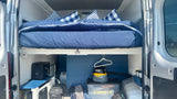 Spacious RV rental interior: raised bed with blue bedding and organized under-bed storage for essential camper van gear.