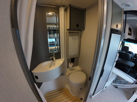 This RV rental offers a compact bathroom with a modern sink, toilet, shower with wooden slats, and reflections of the vehicle's front.