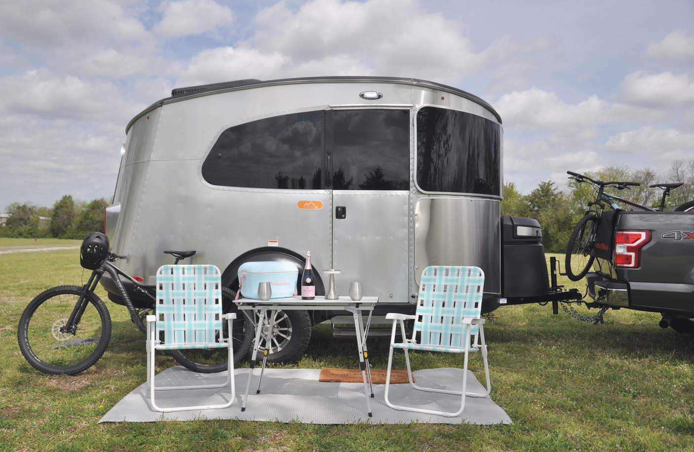 Silver Airstream Basecamp RV rental at a campsite with chairs, table, drinks, and mountain bikes ready for adventure.