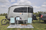 Silver Airstream Basecamp RV rental at a campsite with chairs, table, drinks, and mountain bikes ready for adventure.