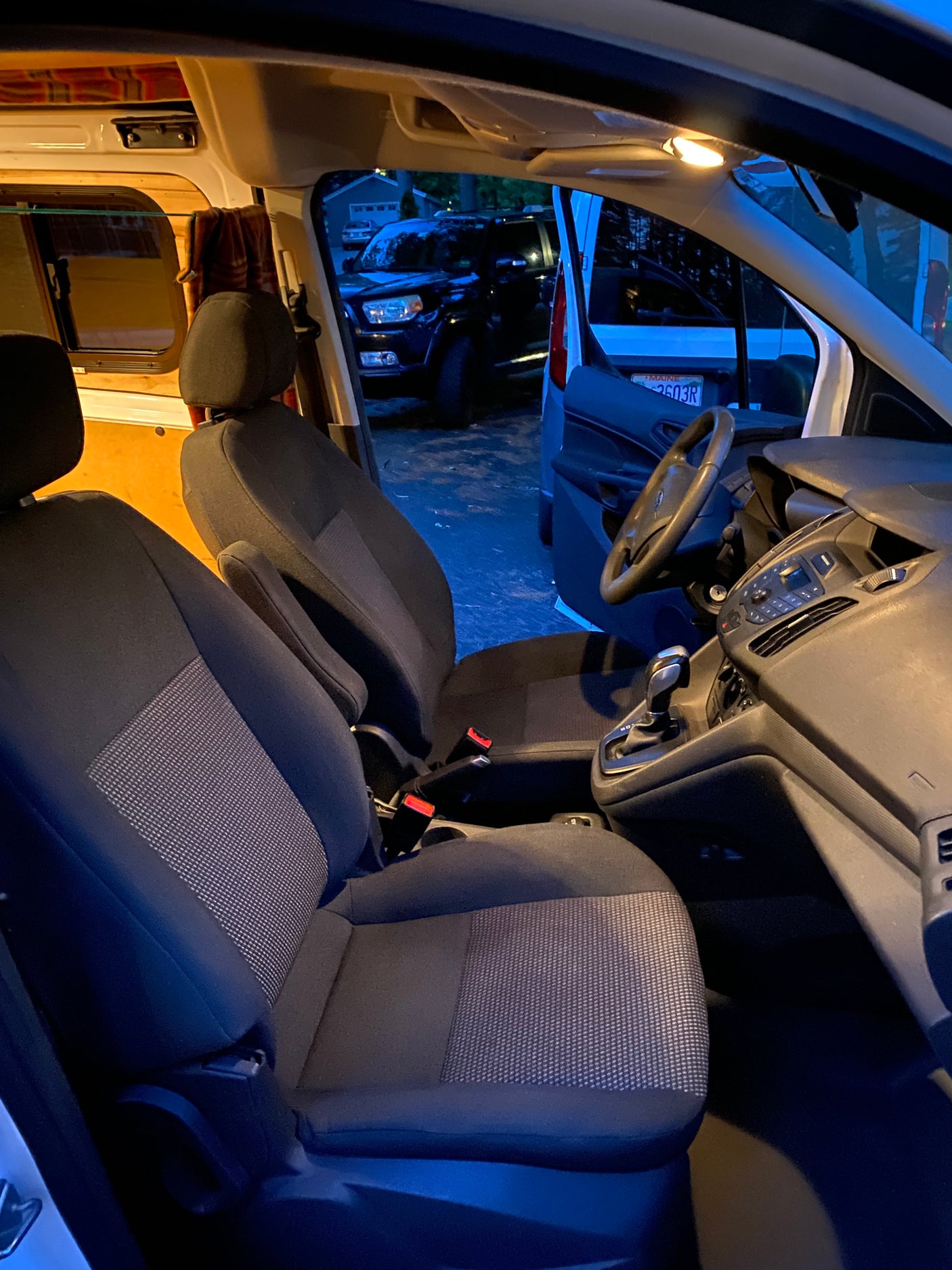 View from inside an RV rental van at dusk. Shows the front cabin, seats, dashboard, and a glimpse of the camper conversion.