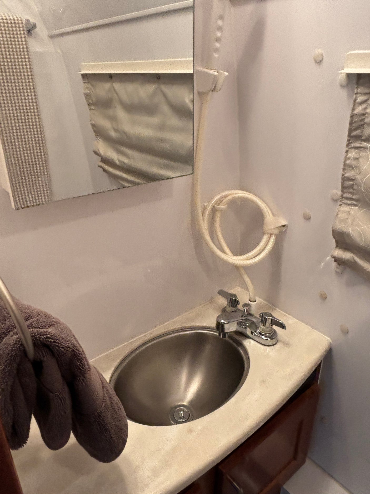 Compact RV rental bathroom: stainless steel sink, chrome faucet, mirror, and handheld shower hose on white walls.