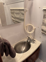 Compact RV rental bathroom: stainless steel sink, chrome faucet, mirror, and handheld shower hose on white walls.