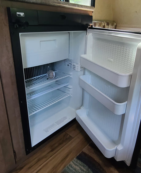 Clean RV rental refrigerator, open to reveal shelves, a small freezer, and door storage, with a thermometer on a shelf.