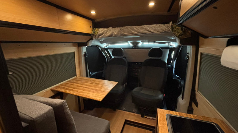  and front seats in a custom camper van conversion.|Modern RV rental interior with a cozy bed — photo 5