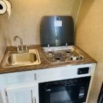 RV rental kitchenette with a sink, two-burner stove (cover open), and microwave below. Compact cooking for your travels. — photo 7