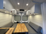 This rv rental shows a bright, modern interior with white plank walls, a cozy gray dinette area, and wooden countertops.