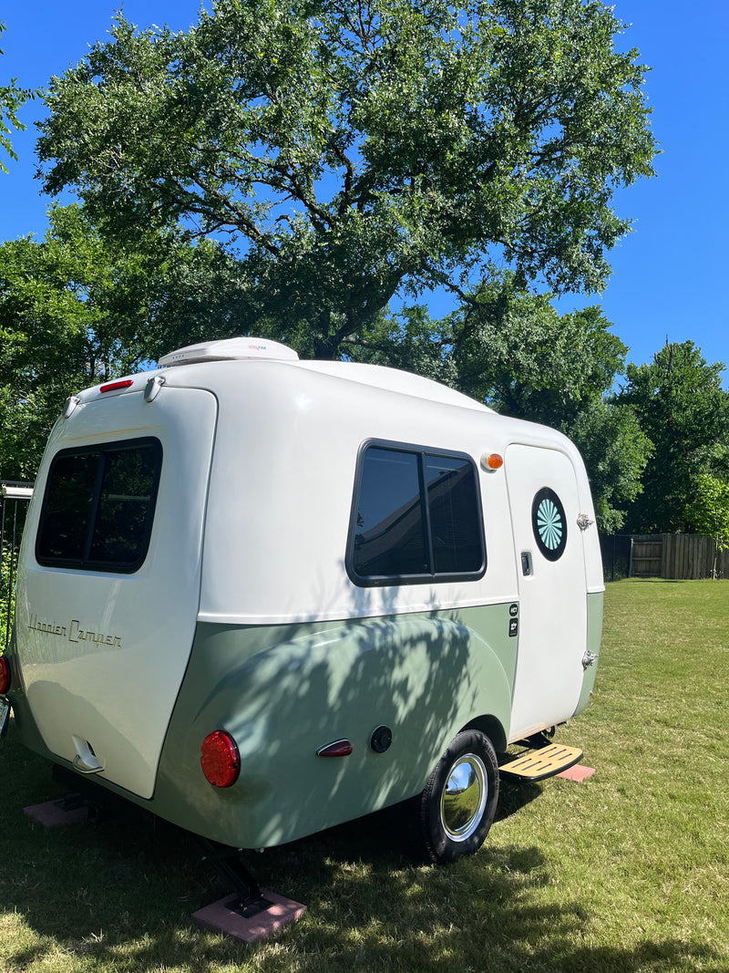 This vintage-style Happier Camper travel trailer is ready for your RV rental, sitting on grass under green trees. — photo 1