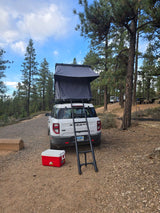 RV rental: A white Bronco Sport with a rooftop tent & ladder, parked at a forested campsite with a cooler.