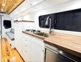 Custom-built rv rental interior: wood-accented kitchen with stove, sink, fridge & bench seating, bright & functional.
