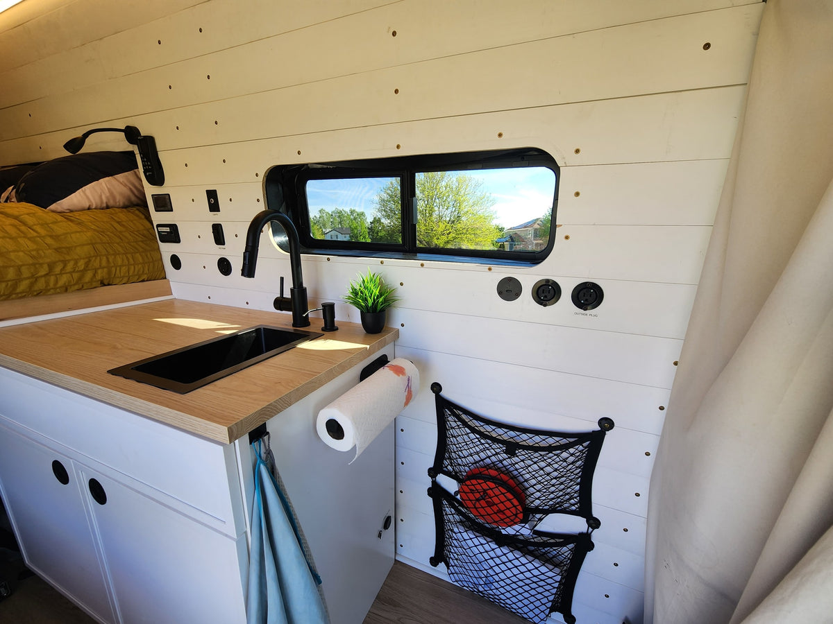 RV rental van's custom kitchenette: black sink, wood counter, wall controls, and practical storage net. — photo 7